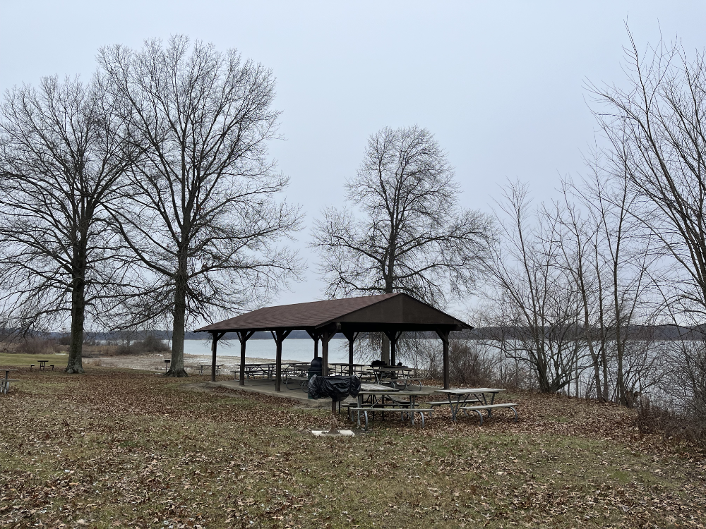 Picnic shelter surrounded by tables and a grill wrapped in plastic.