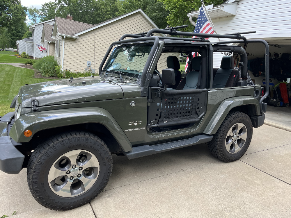 A green Jeep Wrangler with safari doors, a cargo cage, and a soft top with no windows.