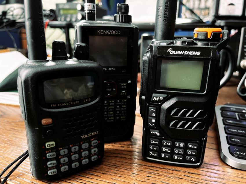 Three handheld amateur radios on a desk.