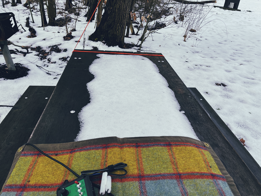 A wet picnic table with an island of crusty ice on its surface. A tarp is resting on the ice at the bottom of the image. 